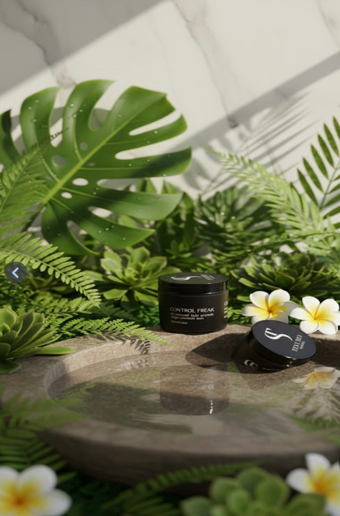 Two black containers on a stone surface with green foliage and flowers in the background