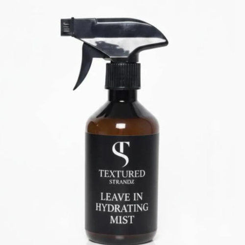 Black spray bottle labeled 'Textured Strandz Leave In Hydrating Mist' on a white background